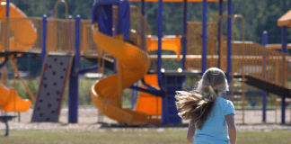 Little girl running towards a blue and yellow playground