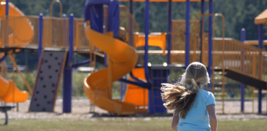 Little girl running towards a blue and yellow playground