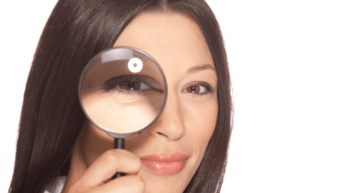 A lady holding up a magnifying glass to one eye.