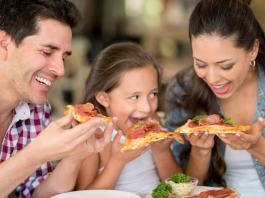 A mom, dad, and daughter eating pizza and smiling together.