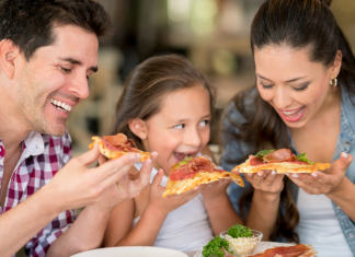 A mom, dad, and daughter eating pizza and smiling together.