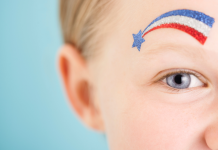 A little boy with blue eyes with a blue star and red, white, and blue stripe over his eye.