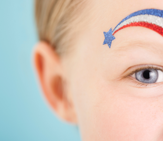 A little boy with blue eyes with a blue star and red, white, and blue stripe over his eye.