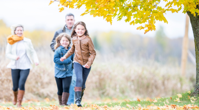 A family with two elementary school age children running under a beautiful yellow tree in fall.