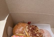 a box filled with half a dozen donuts of various flavors with toppings such as rainbow sprinkles, captain crunch cereal, and crumbled bacon
