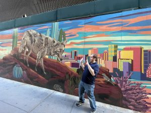 Man in jeans pretending to be scared in front of a mural featuring a desert landscape and large coyote
