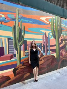 woman in a black dress standing in front of a city scape mural with cacti